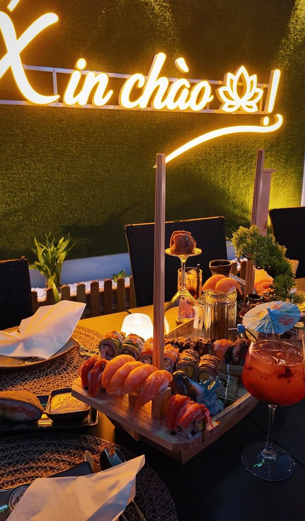 Romantisch gedeckter Tisch im Freien bei Abenddämmerung mit einem bootsförmigen Sushi-Tablett, Kerzenlicht und Lichterketten im Hintergrund